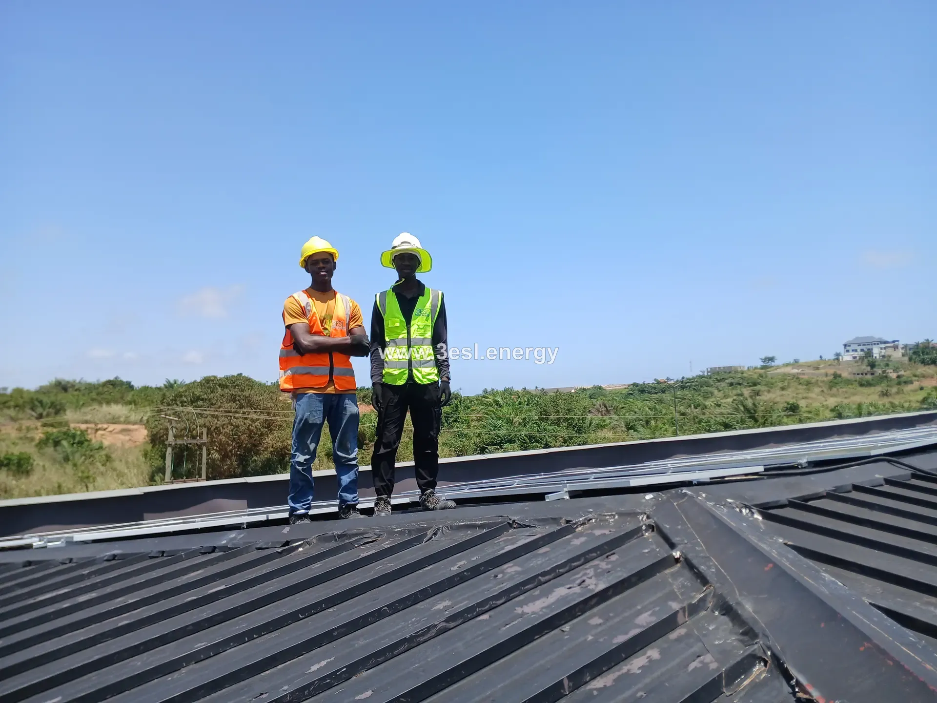 Two 3ESL crew members standing on a completed rooftop array in hard hats and high-visibility vests.