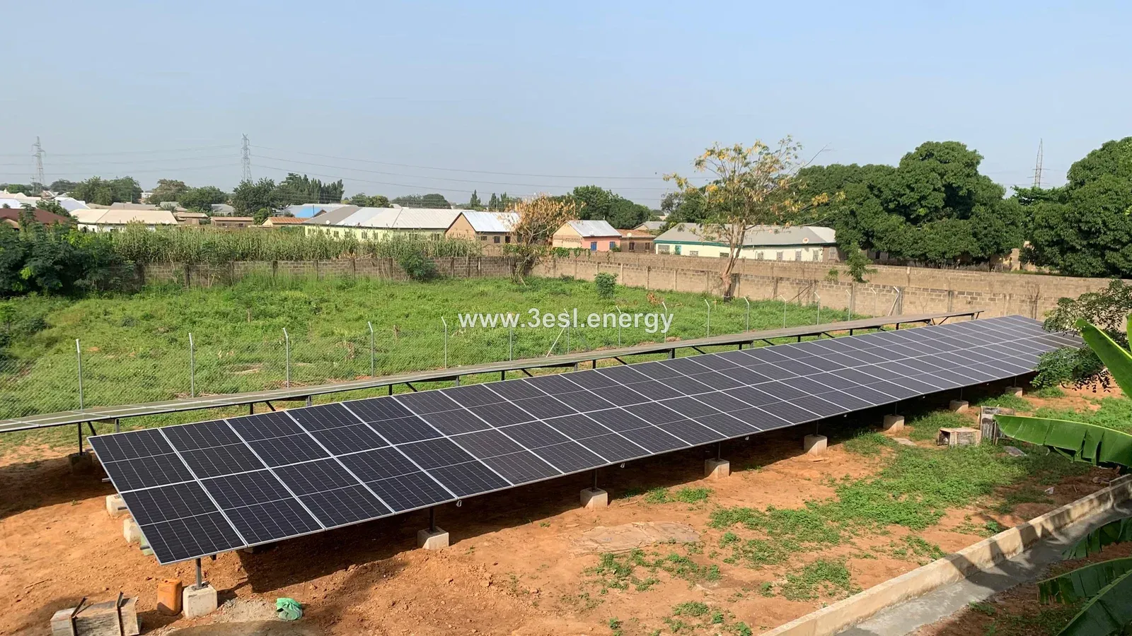 A ground-mounted solar array on concrete supports beside a fenced green field.