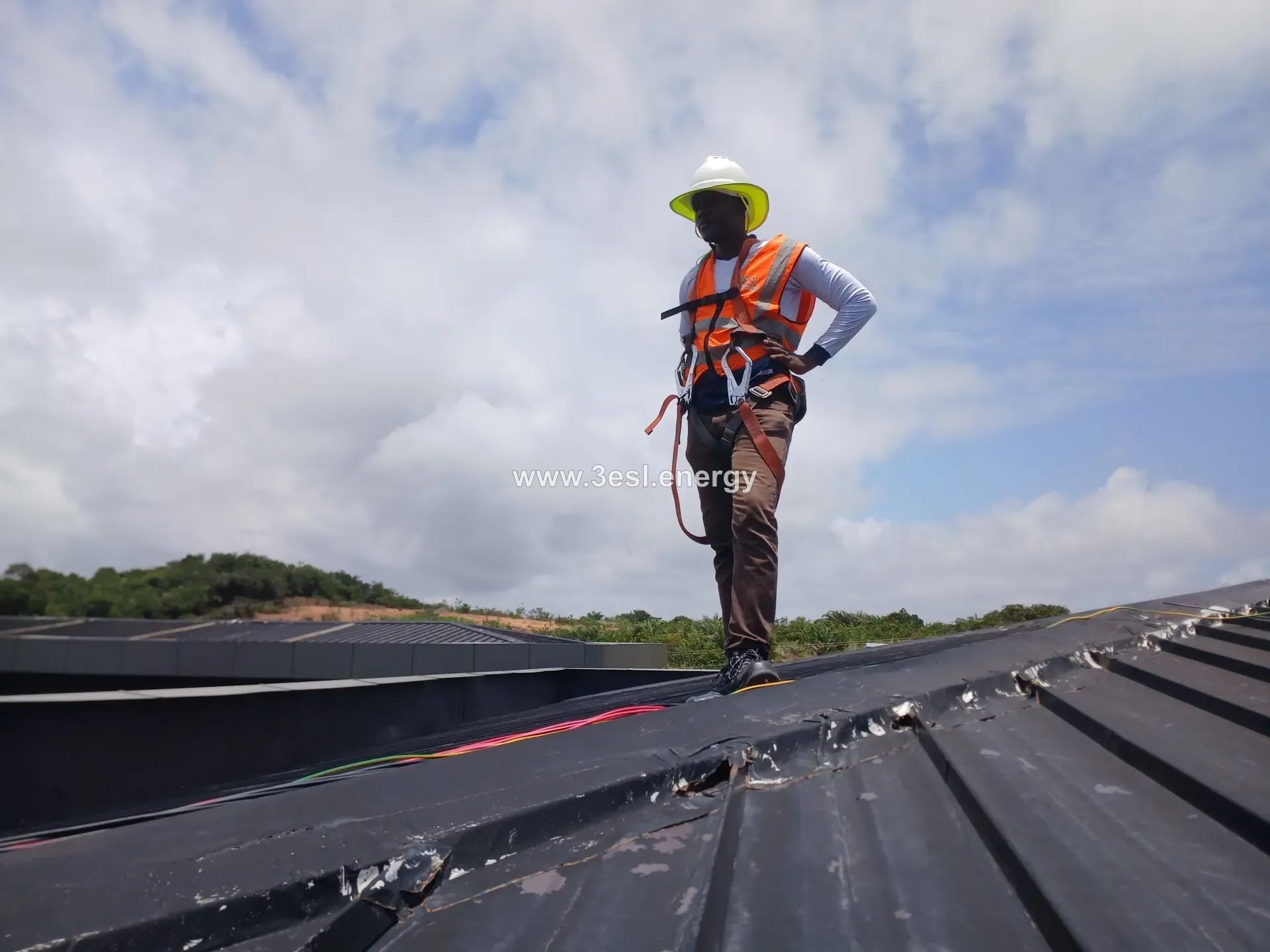 A 3ESL technician in a full-body safety harness walking a commercial standing-seam metal roof.
