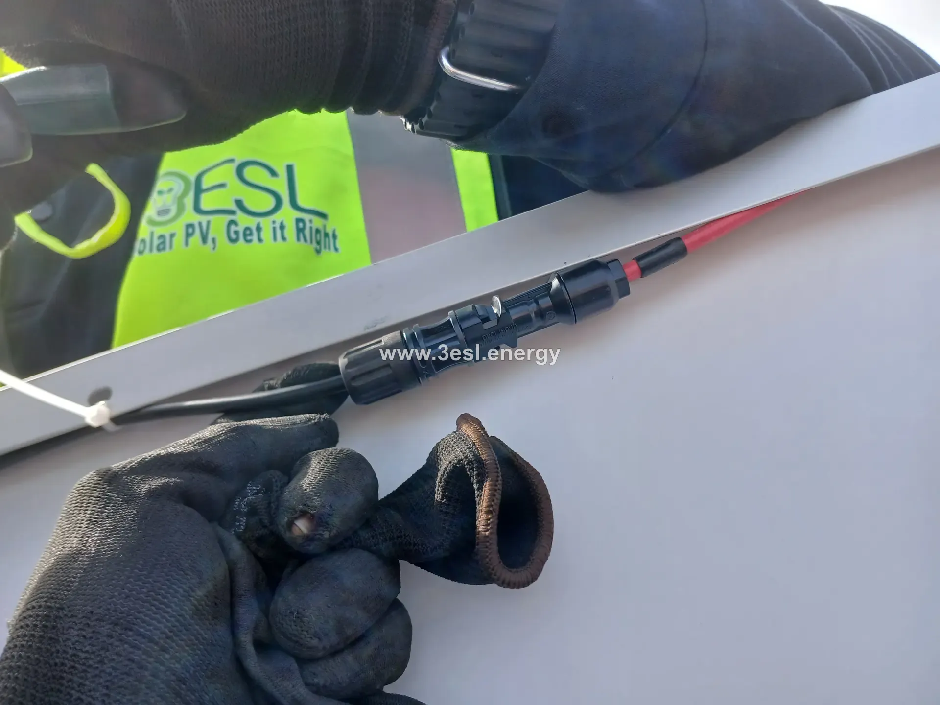 Close-up of gloved hands crimping an MC4 photovoltaic connector, a 3ESL vest visible behind.