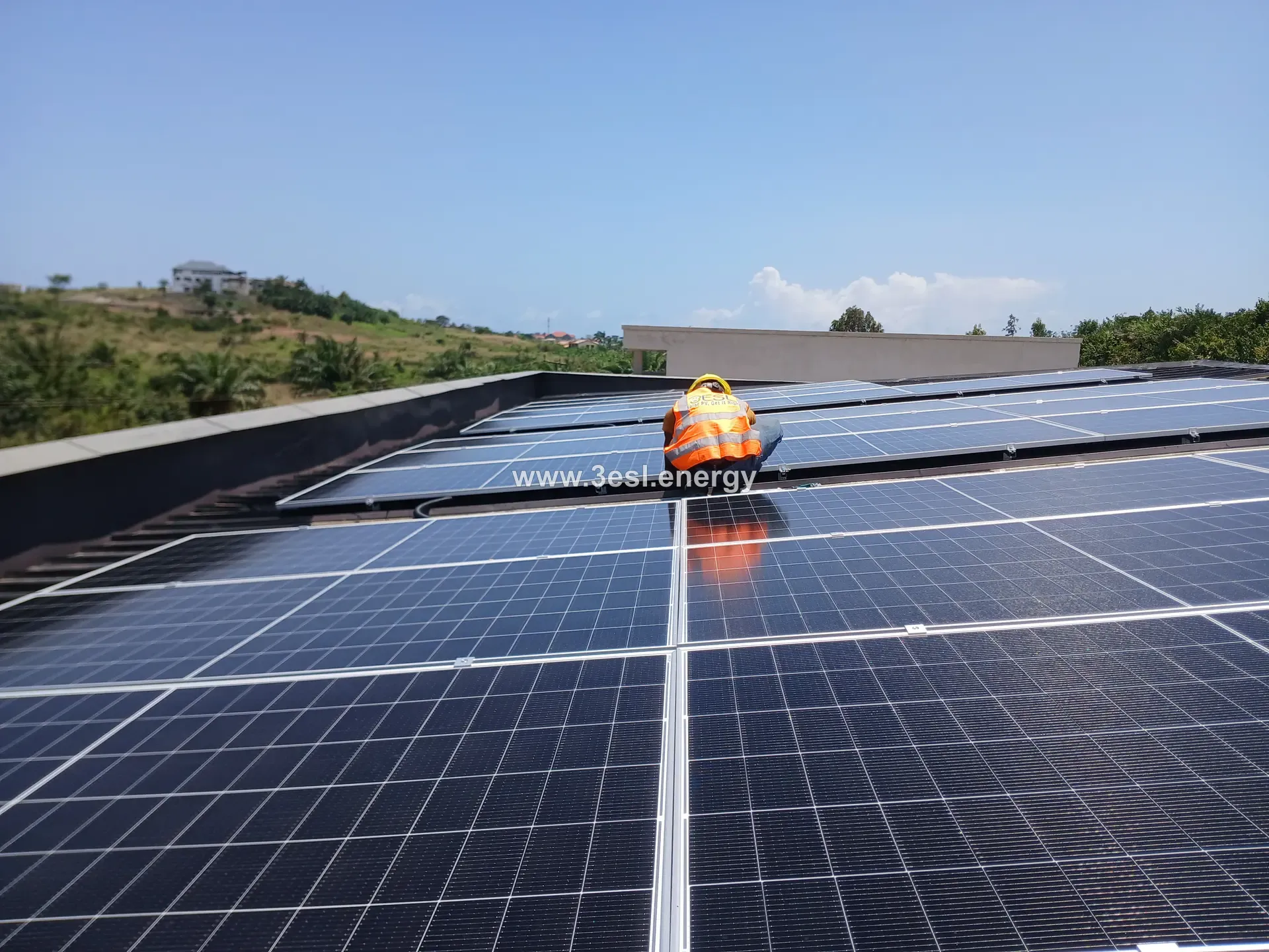 A technician kneeling to position a photovoltaic module onto a roof-mounted rail.