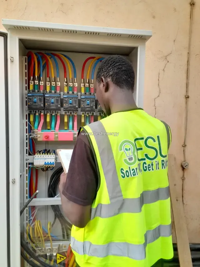 A technician in a 3ESL high-visibility vest working inside an open distribution board full of coloured cabling.