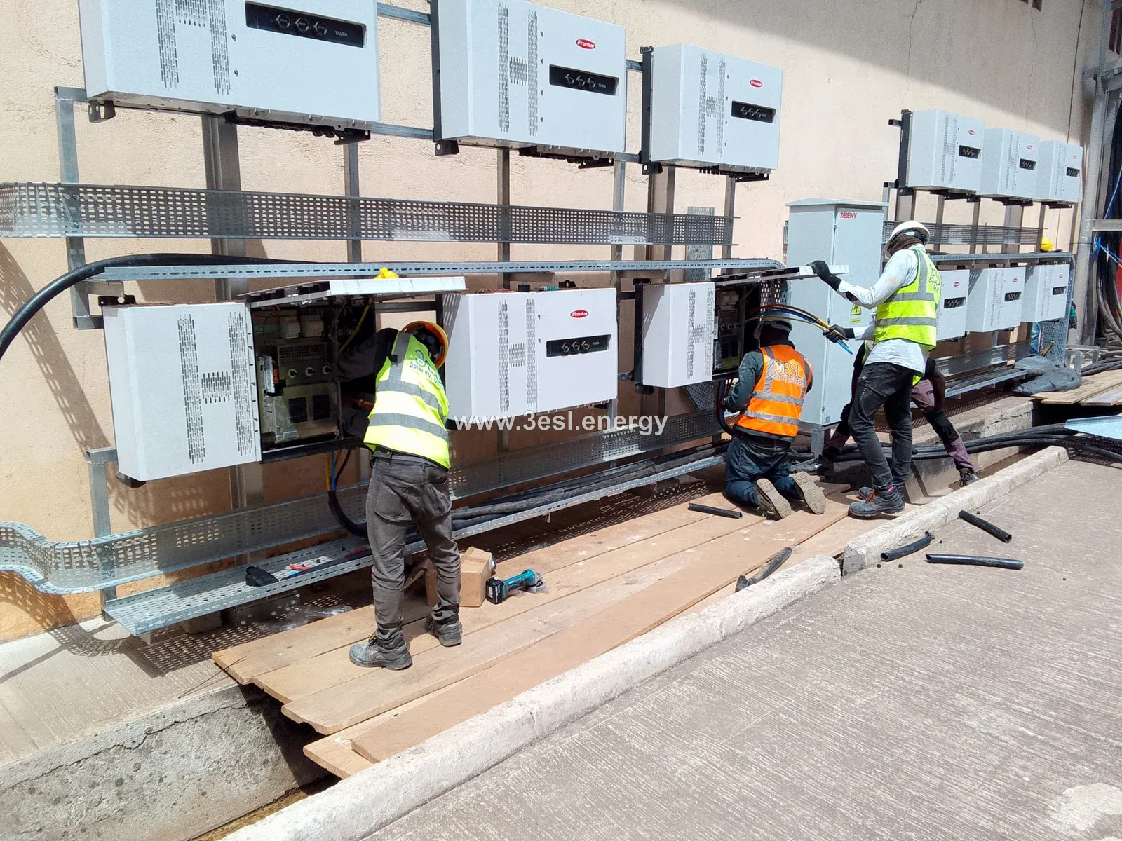 Technicians installing and wiring a bank of industrial solar inverters.
