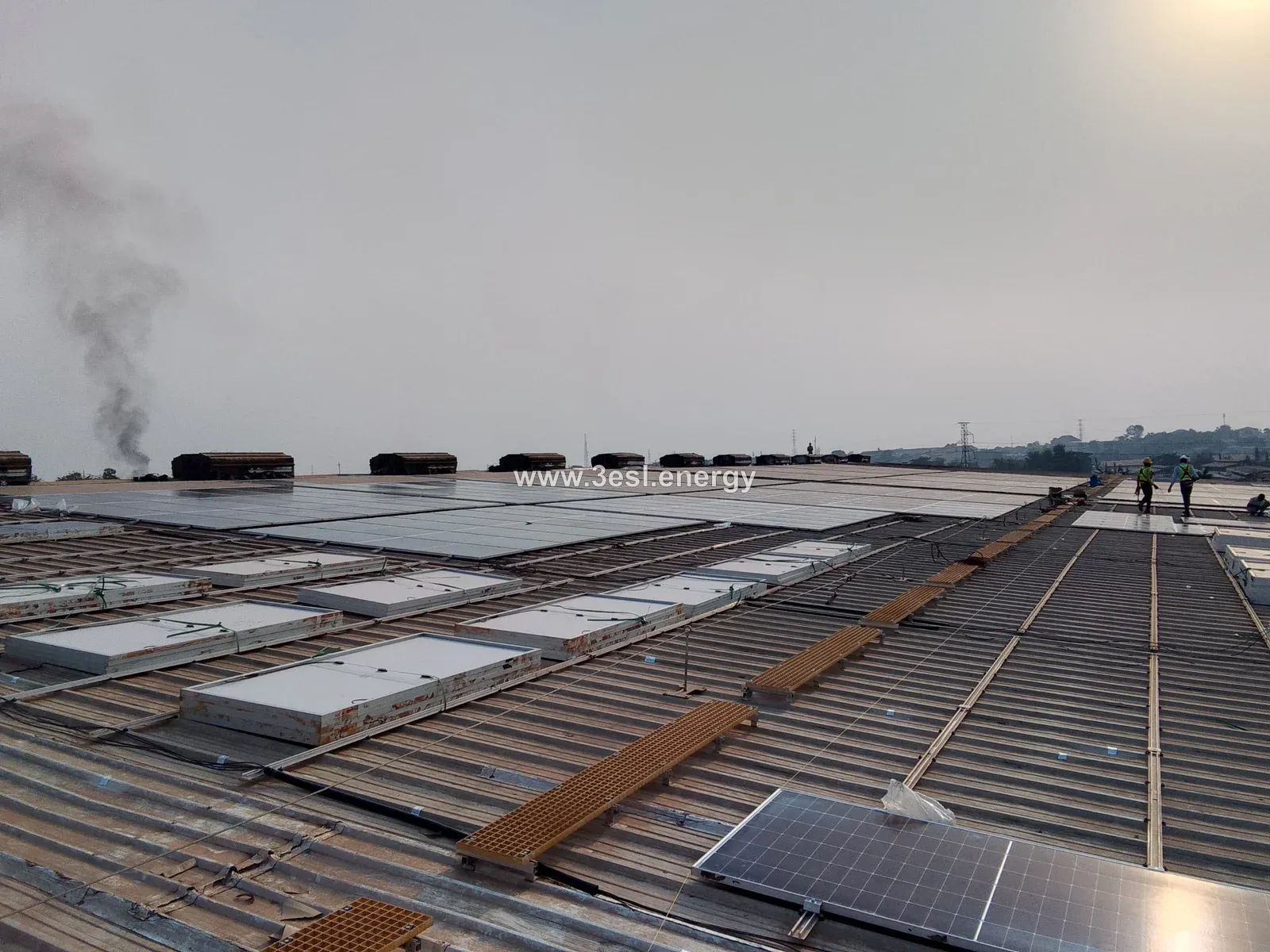 An industrial rooftop solar installation in progress, with module rows, mounting rails and a maintenance walkway.
