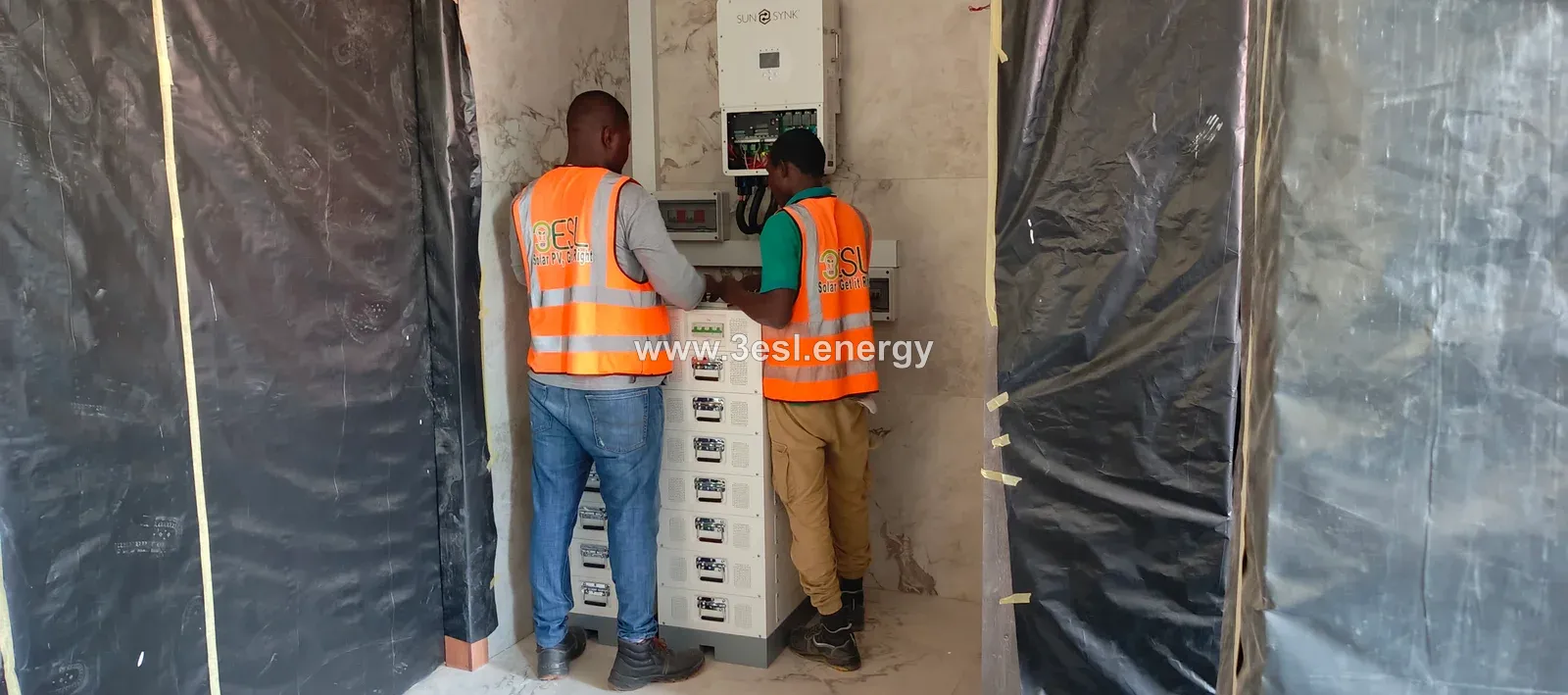 Two technicians commissioning a hybrid inverter and a stack of lithium batteries.