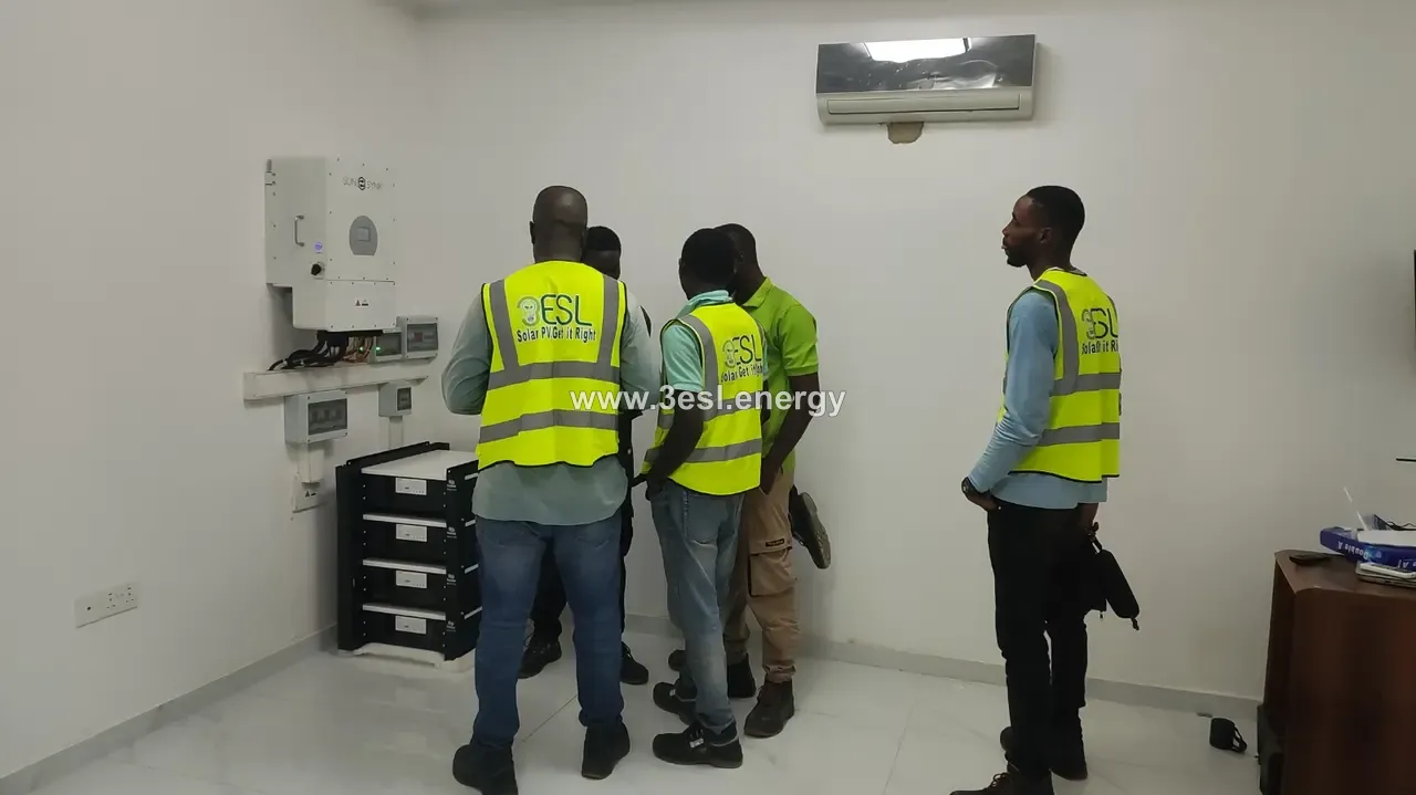 Three technicians in high-visibility vests reviewing a newly installed battery bank and inverter.