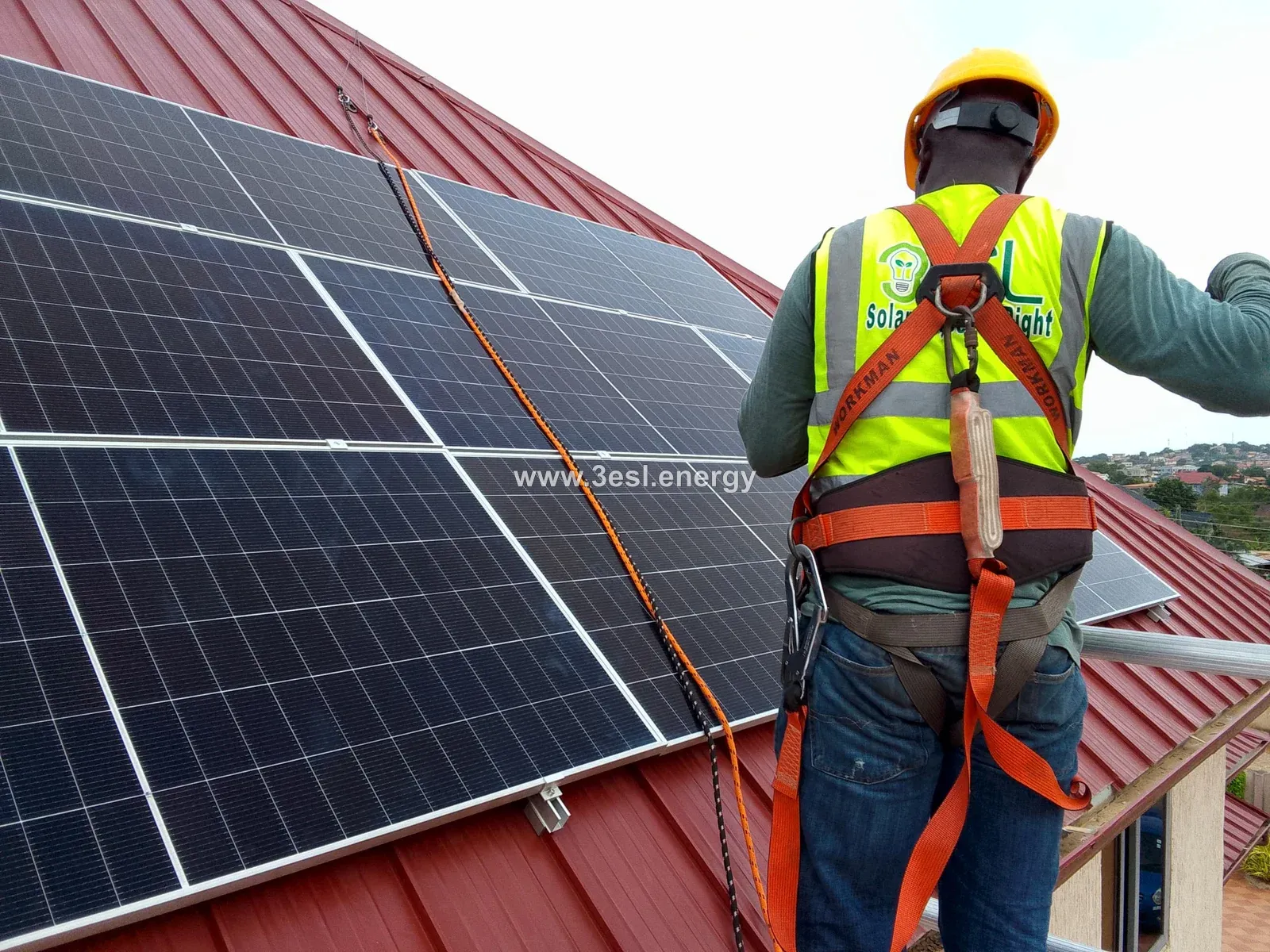An installer wearing a harness beside solar panels on a red pitched roof.