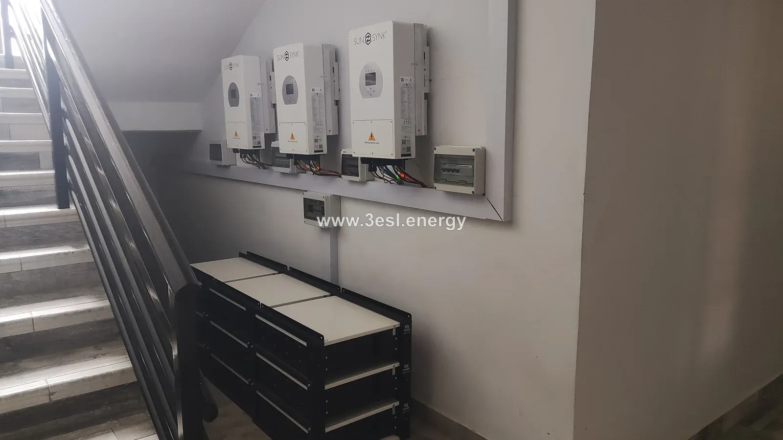 Three Sunsynk inverters and a battery bank installed beside a staircase.