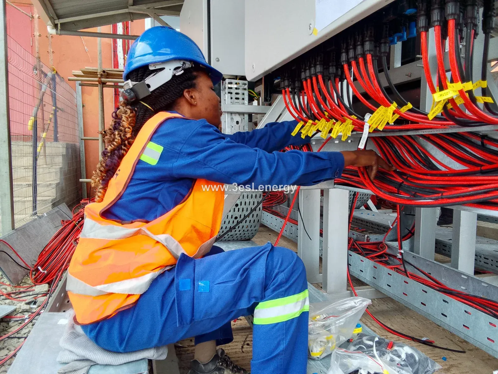 A technician arranging labelled solar cables beneath an inverter bank.