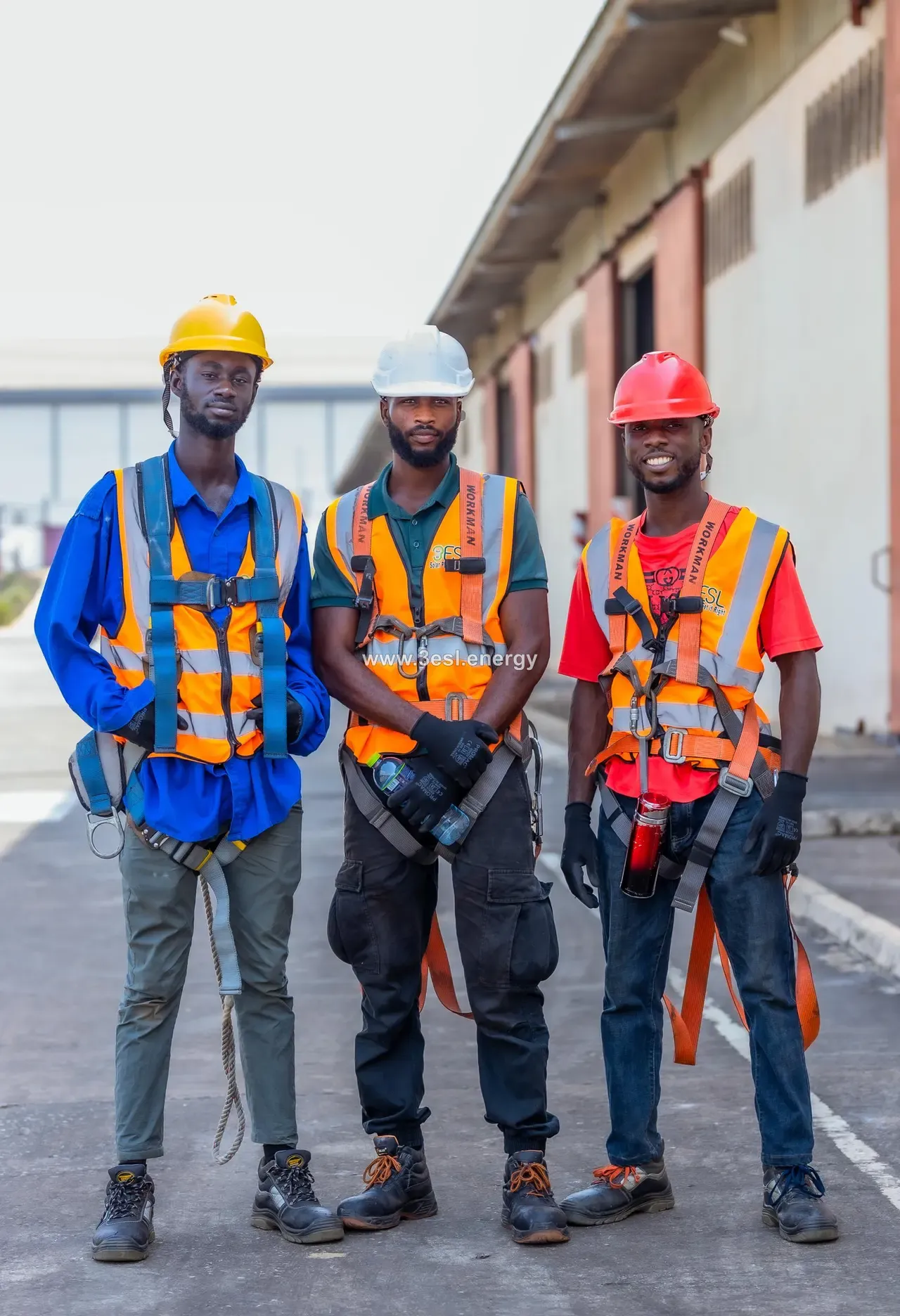 Three 3ESL technicians in high-visibility vests and fall-arrest harnesses standing together on site.