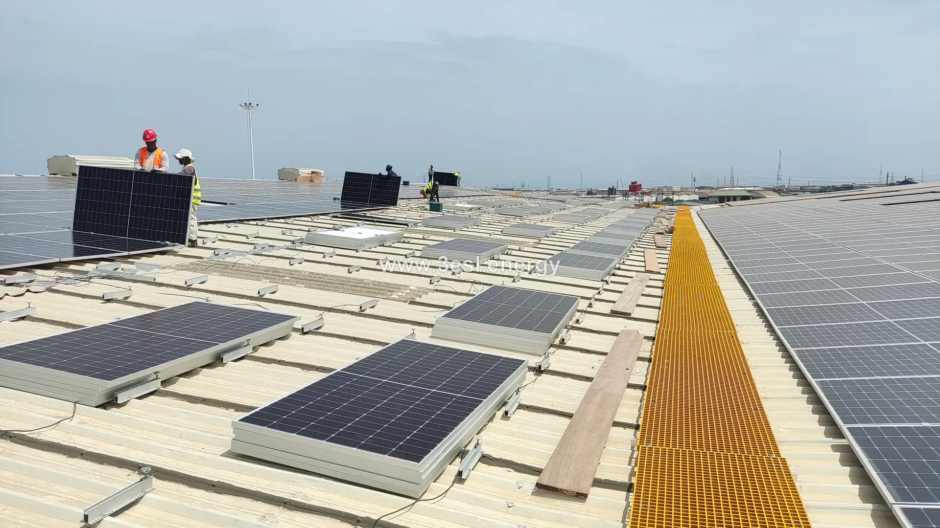 Row upon row of solar modules across a very large industrial roof under a pale sky.