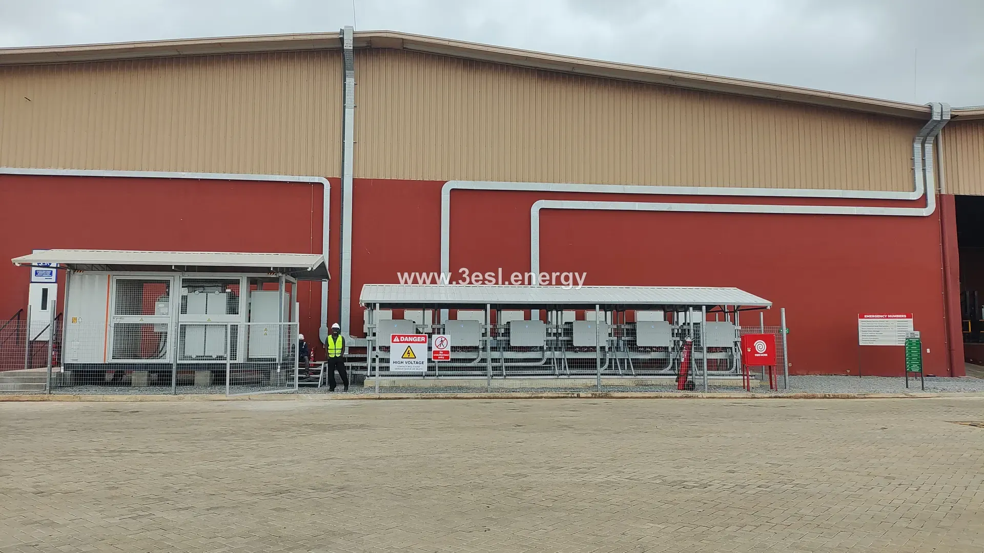 A large red and white industrial building with a solar array running along its roofline.